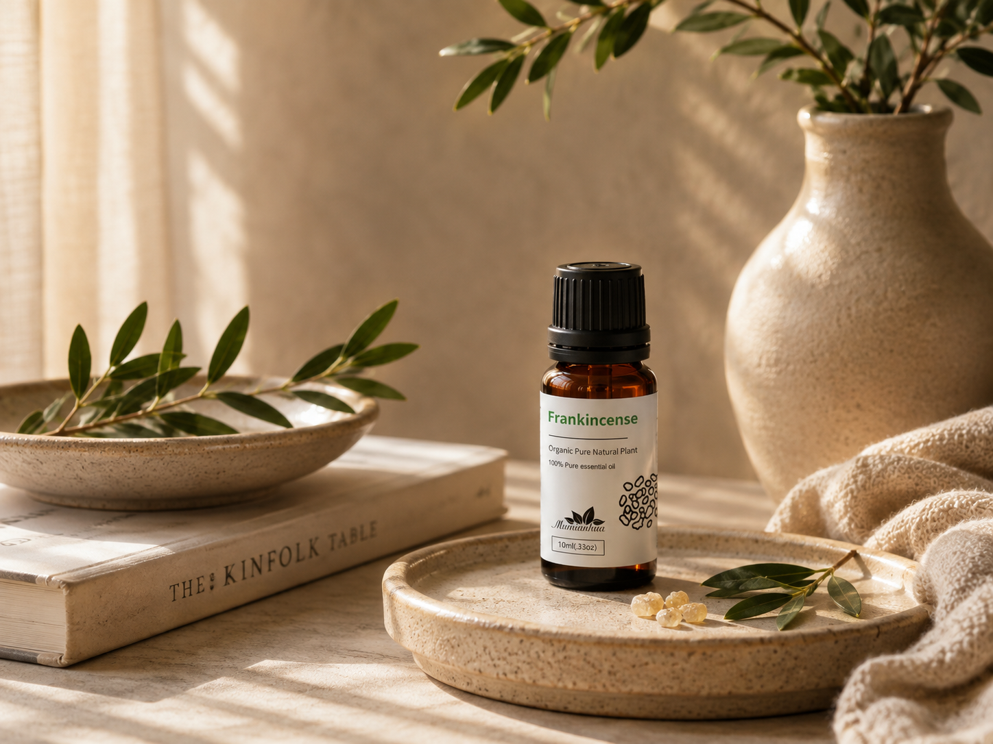 Frankincense essential oil bottle with white botanical packaging on a ceramic dish beside olive leaves in soft daylight
