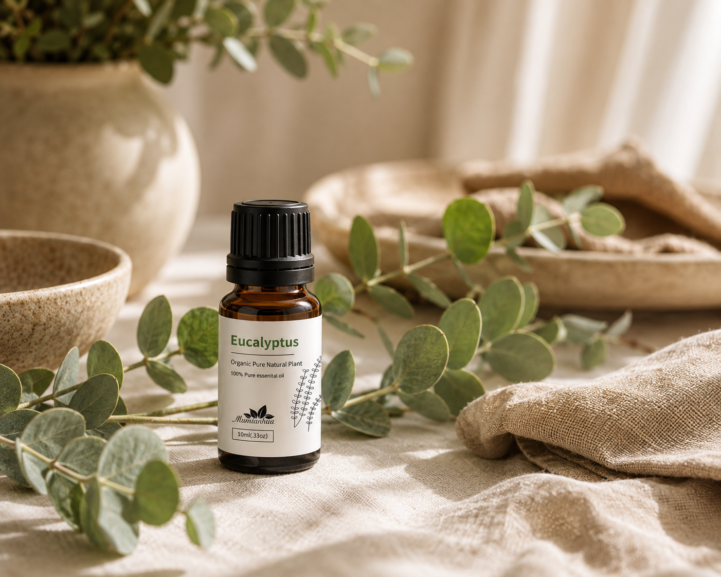 A Eucalyptus amber essential oil bottle with a white botanical label and black ribbed cap resting on warm cream linen with fresh eucalyptus branches and neutral ceramics in soft natural light