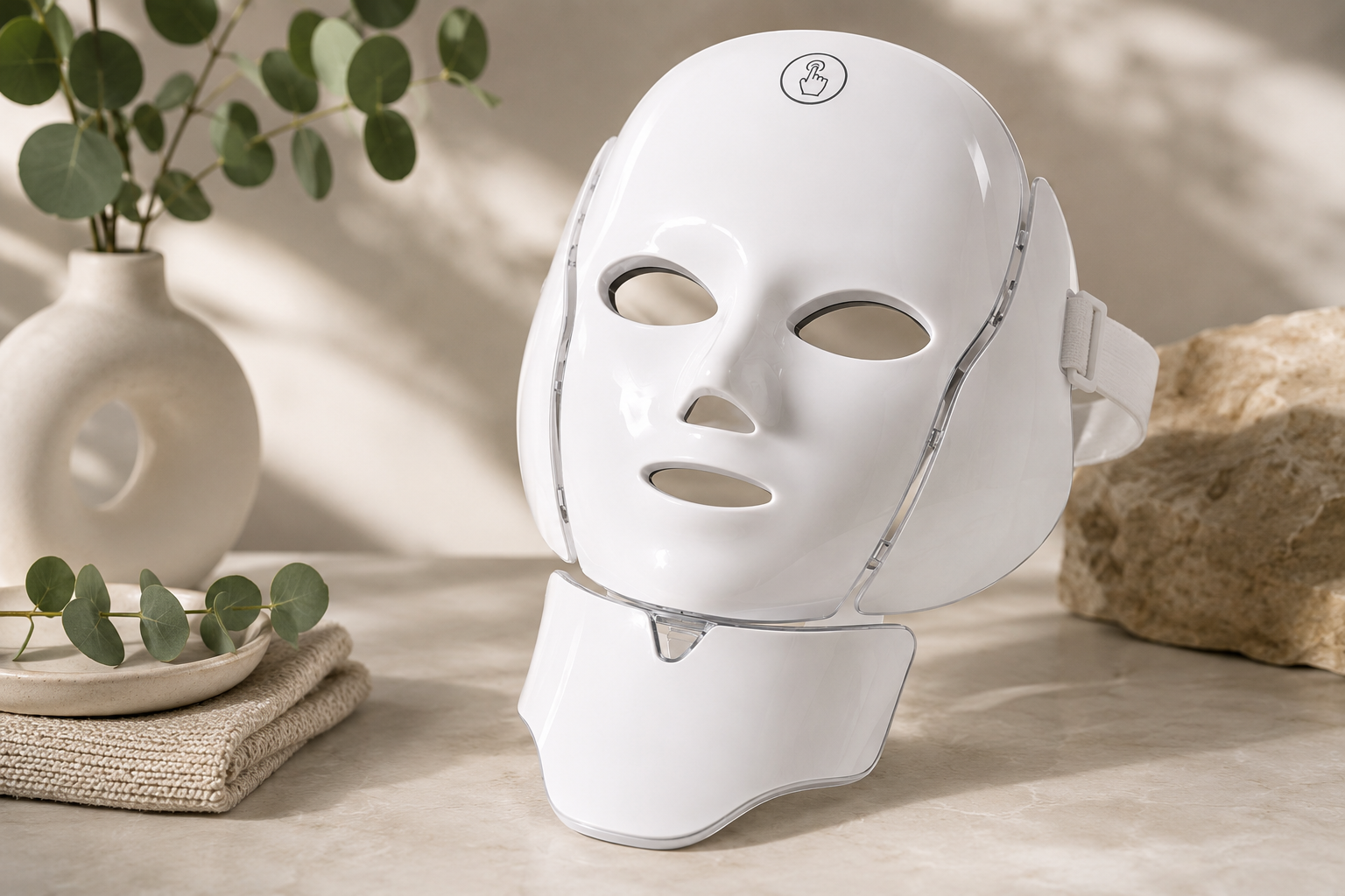 The Wellthious Luma Ritual Face + Neck Mask — a glossy white LED face and neck mask with separate neck panel in a warm neutral setting