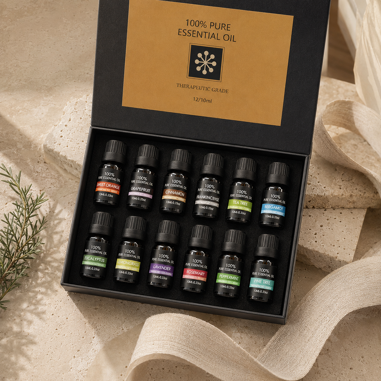 Twelve-bottle essential oil discovery set presented in a black and gold gift box on warm stone with natural linen.